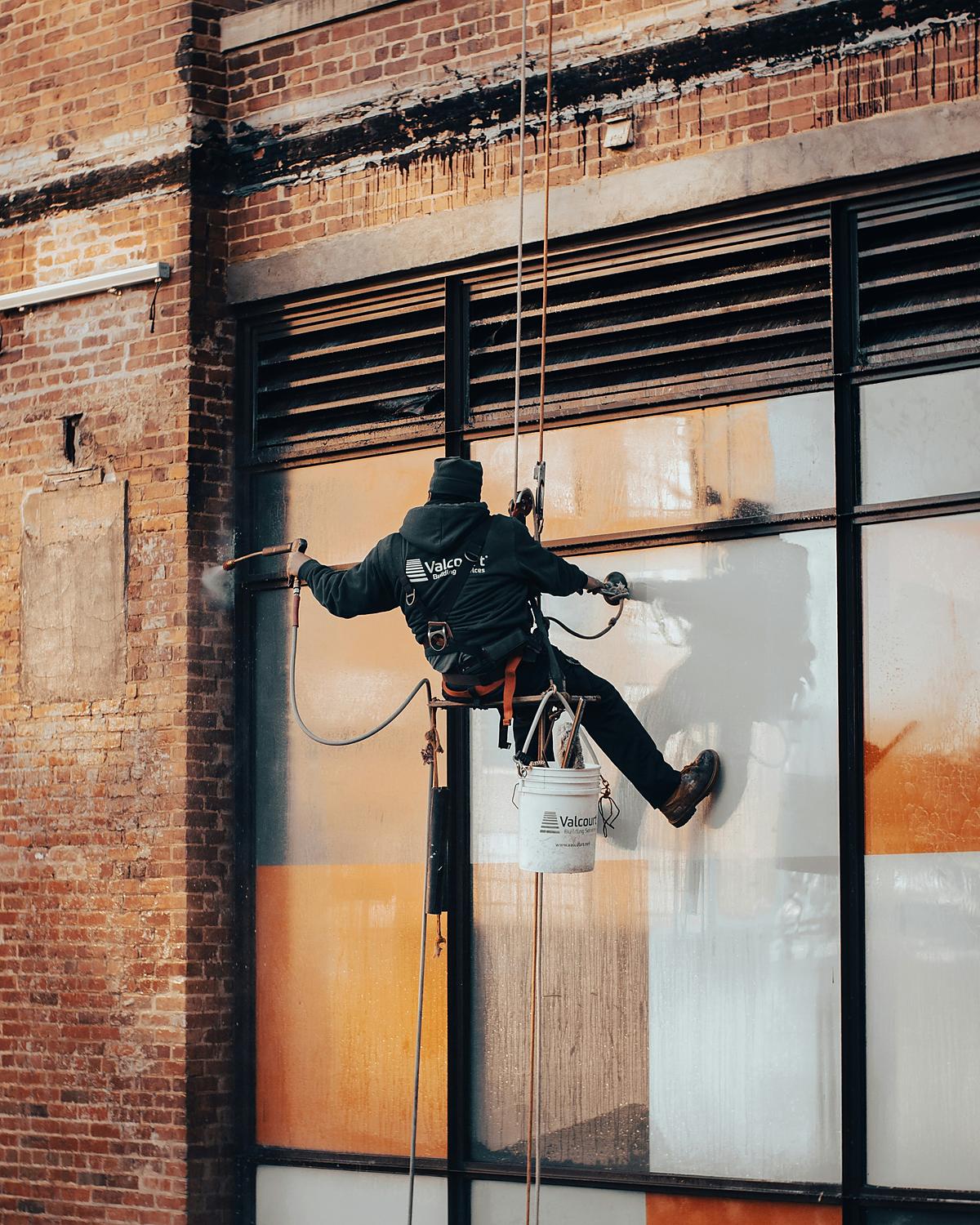 Rope-access cleaner with a bucket cleaning a brick window at height