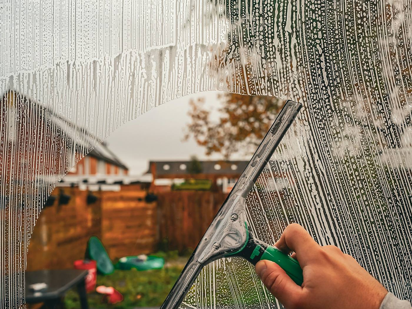 Hand pulling a squeegee across a soapy window